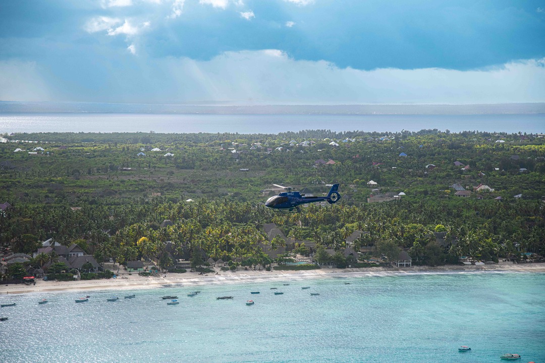 A blue helicopter flying across an island in Zanzibar